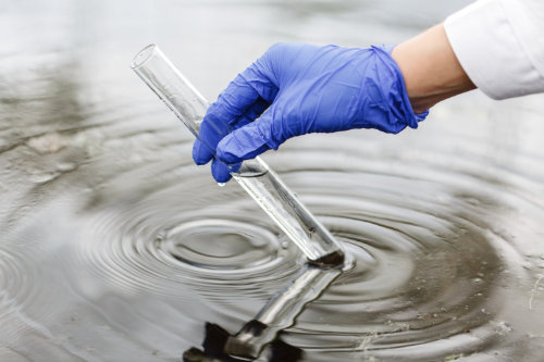 mano con guante tomando muestra de agua con tubo de laboratorio